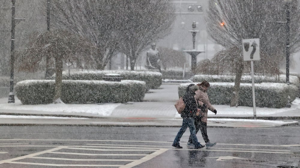 The snow Friday, Feb. 16, 2024 partially obscures two people as they cross Fountain Avenue in downtown Springfield. BILL LACKEY/STAFF