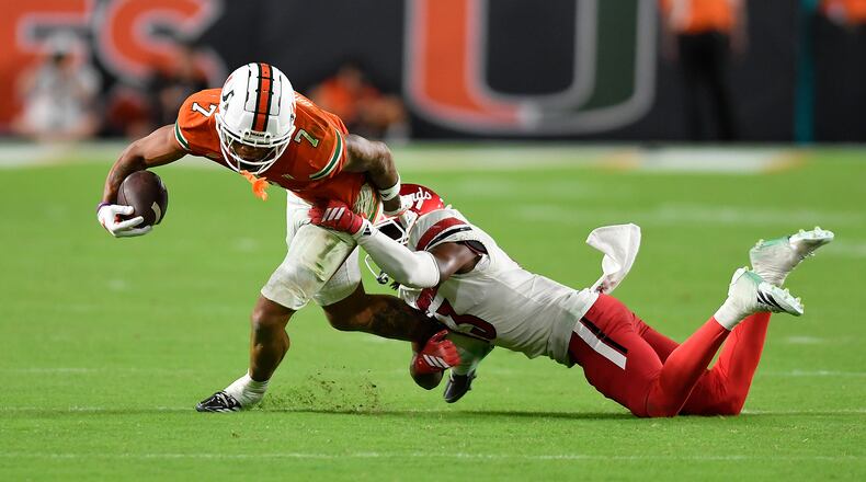 Miami wide receiver CJ Daniels (7) is tackled by Louisville cornerback Justin Agu during the second half of an NCAA college football game, Friday, Oct. 17, 2025, in Miami Gardens, Fla. (AP Photo/Michael Laughlin)