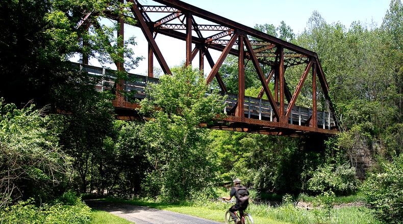 A man rides his bike under the Simon Kenton Trail bridge as he travels along the Buck Creek Trail Wednesday, May 8, 2024. The bridge was built in 1915. BILL LACKEY/STAFF