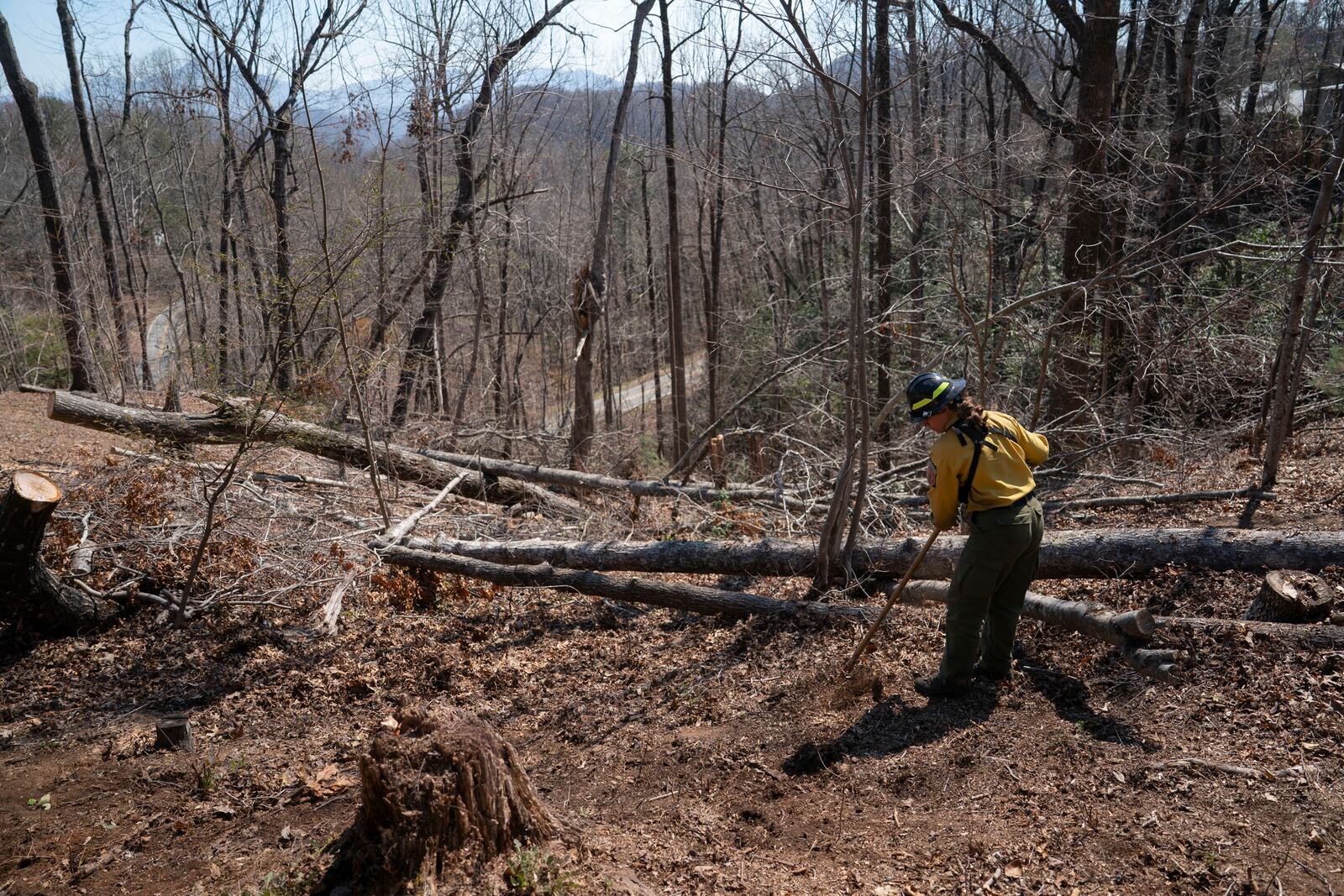 A firefighter works to clear debris from Hurricane Helene to protect a home as the Black Cove Fire burns nearby Wednesday, March 26, 2025, in Saluda, N.C.. (AP Photo/Allison Joyce)