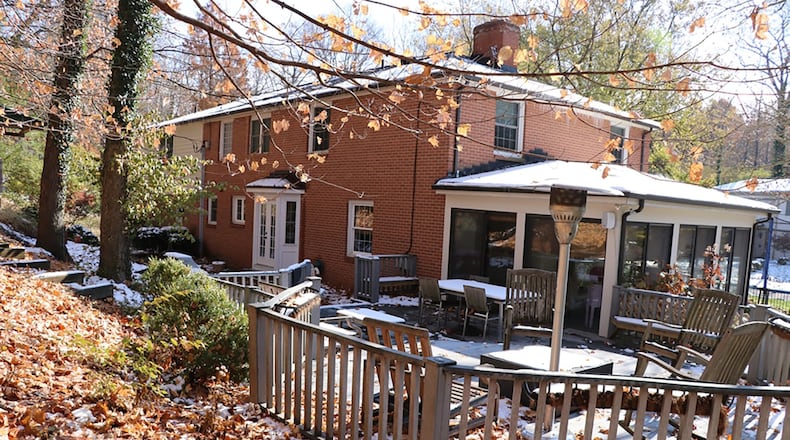 A stone retainer wall edges the length of the backyard patio emphasizing the picturesque and user-friendly outdoor space with a bi-level deck and an additional elevated deck that is built into the adjacent upward-sloping wooded area.