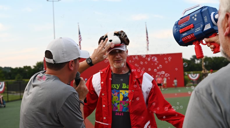 The 12th annual Nuxy Bash, a local celebrity softball game which also features many of the All Stars from the athletes that play at the Joe Nuxhall Miracle League, was held in Fairfield on Saturday, July 27, 2024. Pictured is Reds Community Fund Executive Director Charley Frank celebrating a homerun. The Nuxy Bash took on its own homerun celebration as anyone who hits one gets to wear a Reds jacket and Schottzie hat, which Nuxhall Foundation Executive Director Tyler Bradshaw is placing on Frank's head. Phil Nuxhall is spraying Frank with celebratory bubbles. MICHAEL D. PITMAN/STAFF