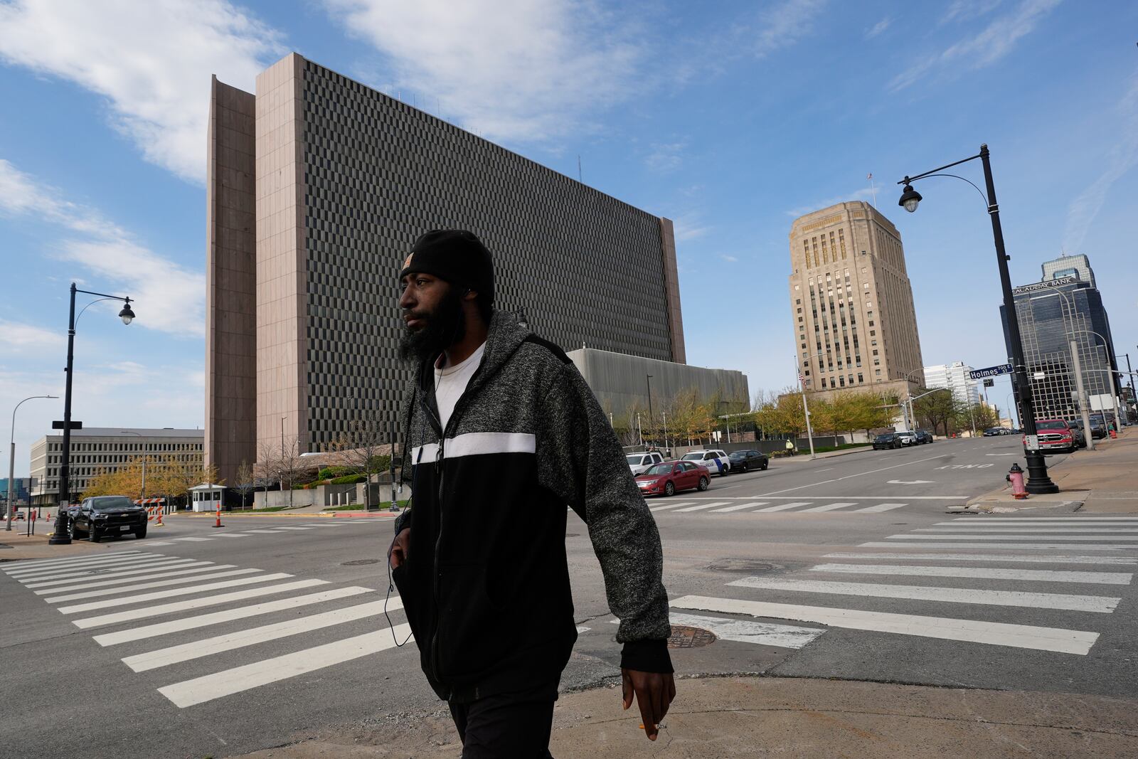 A pedestrian walks past the The Richard Bolling federal building, left, Monday, April 14, 2025, in Kansas City, Mo. (AP Photo/Charlie Riedel)