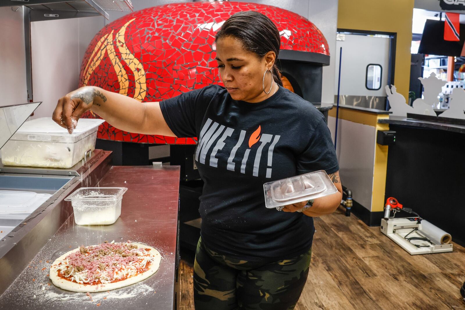 ILLY'S Fire Pizza owner, Kelly Gunn, sprinkles toppings on a pizza before sliding it into the oven at W. Social Tap & Table. JIM NOELKER/STAFF
