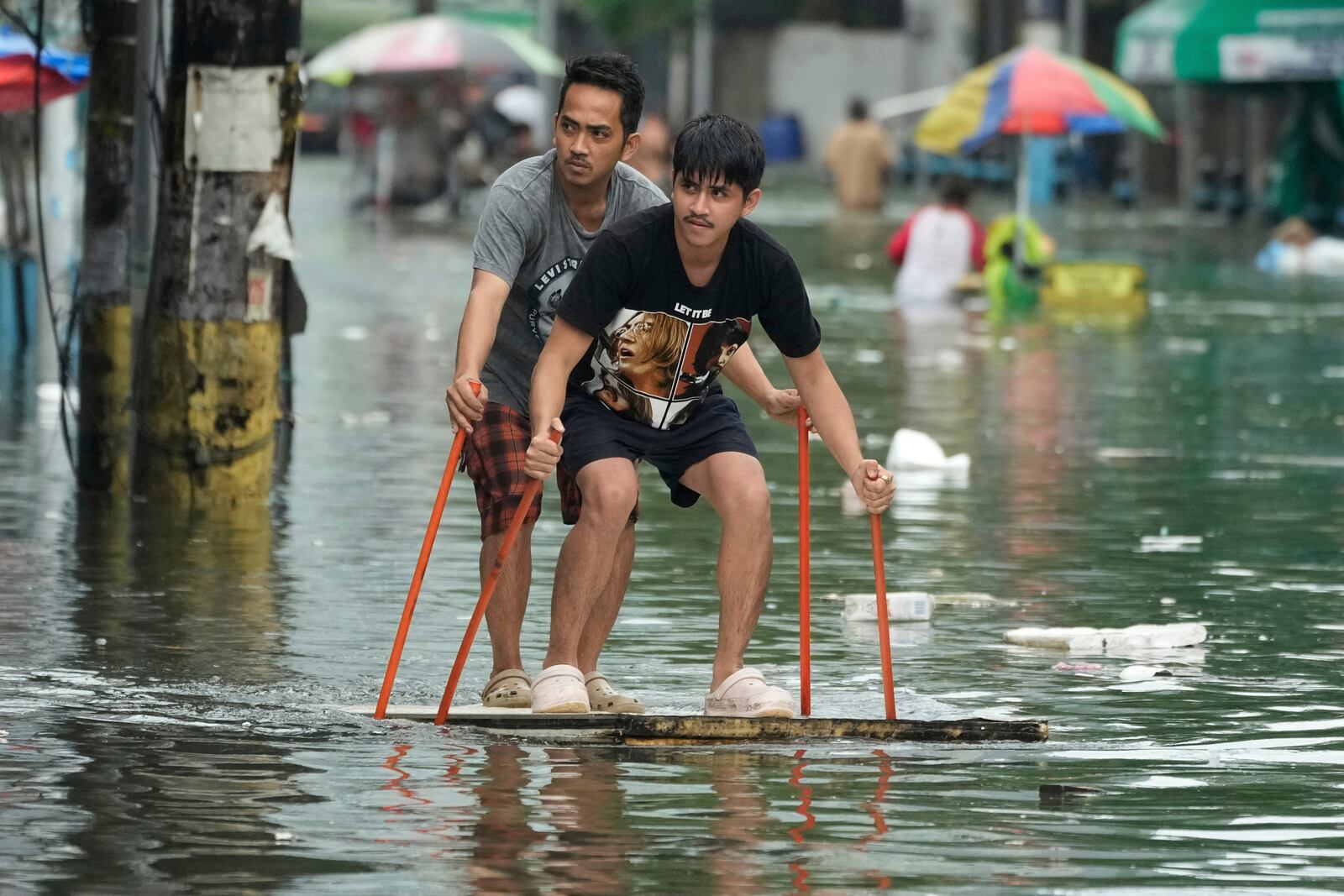 Residents use poles as they ride an improvised float along a flooded road as Typhoon Co-may intensified seasonal monsoon rains at Malabon city, Philippines on Friday, July 25, 2025. (AP Photo/Aaron Favila)