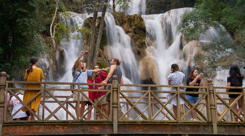 Tourists pose for photos on a footbridge in front of Kuang Si Waterfall near Luang Prabang, Laos, one of the country's most popular natural attractions known for its multi-tiered limestone cascades and turquoise pools on Tuesday, Nov. 4, 2025. (AP Photo/Eugene Hoshiko)