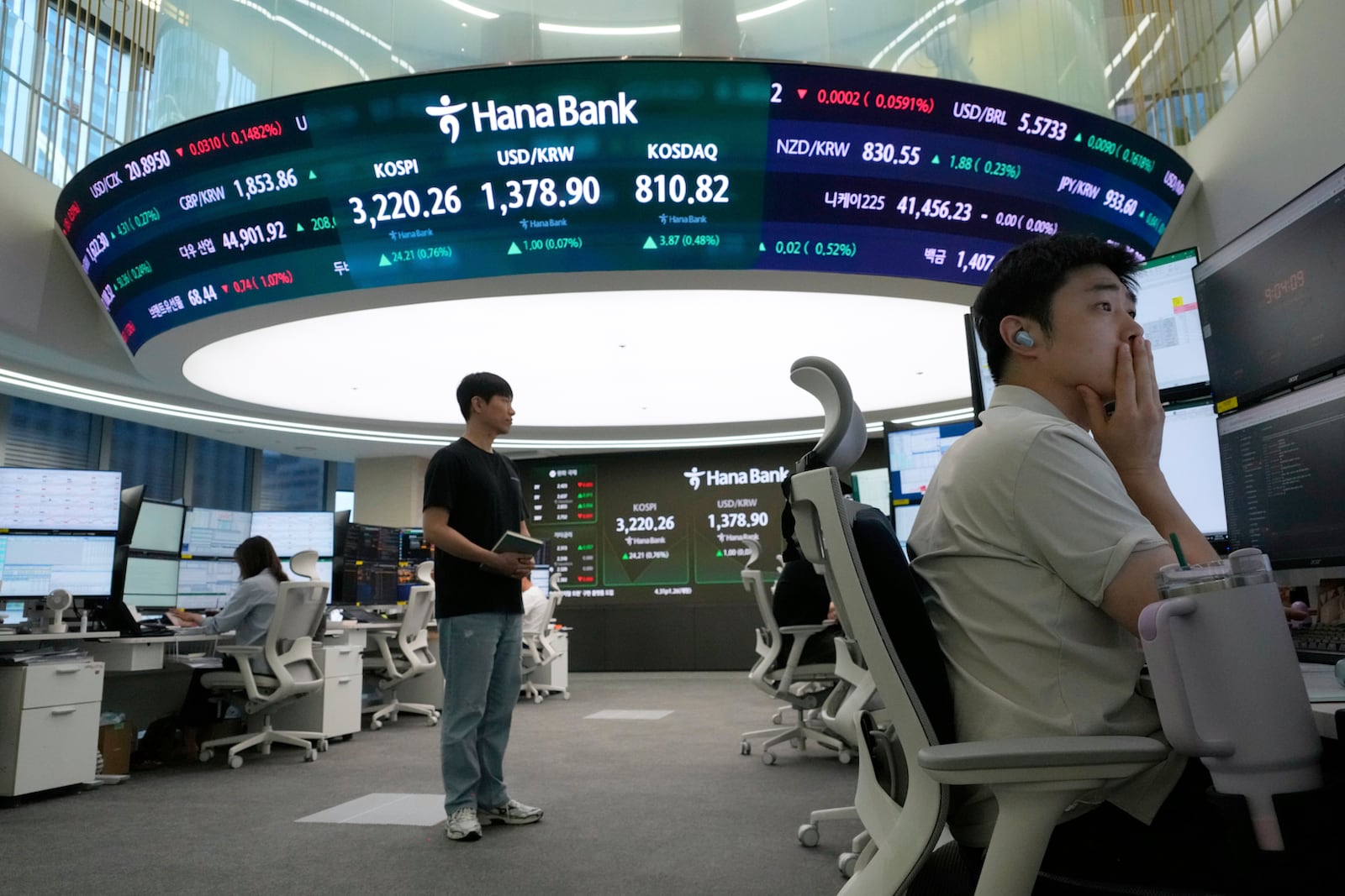 A currency trader watches monitors near a screen showing the Korea Composite Stock Price Index (KOSPI), top center left, and the foreign exchange rate between U.S. dollar and South Korean won, top center, at the foreign exchange dealing room of the Hana Bank headquarters in Seoul, South Korea, Monday, July 28, 2025. (AP Photo/Ahn Young-joon)