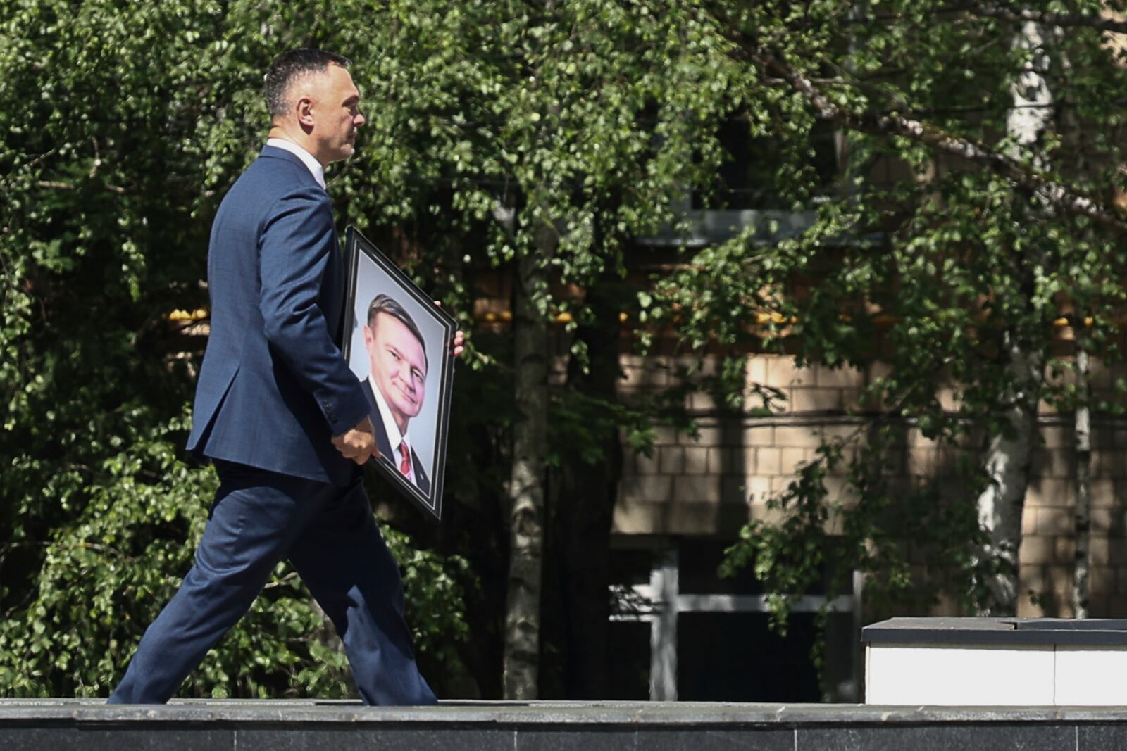 A man carries a portrait of Roman Starovoit, the former transport minister who died in an apparent suicide after his dismissal while people line up to his bid farewell, at the morgue of the Central Clinical Hospital in Moscow, Russia, Thursday, July 10, 2025. (AP Photo)