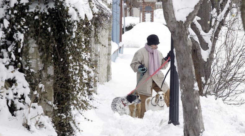 This 2008 photo shows a woman walking around the sidewalk with her three dogs because of almost a foot of snow covers the McPherson Town sidewalks in Dayton. STAFF/FILE