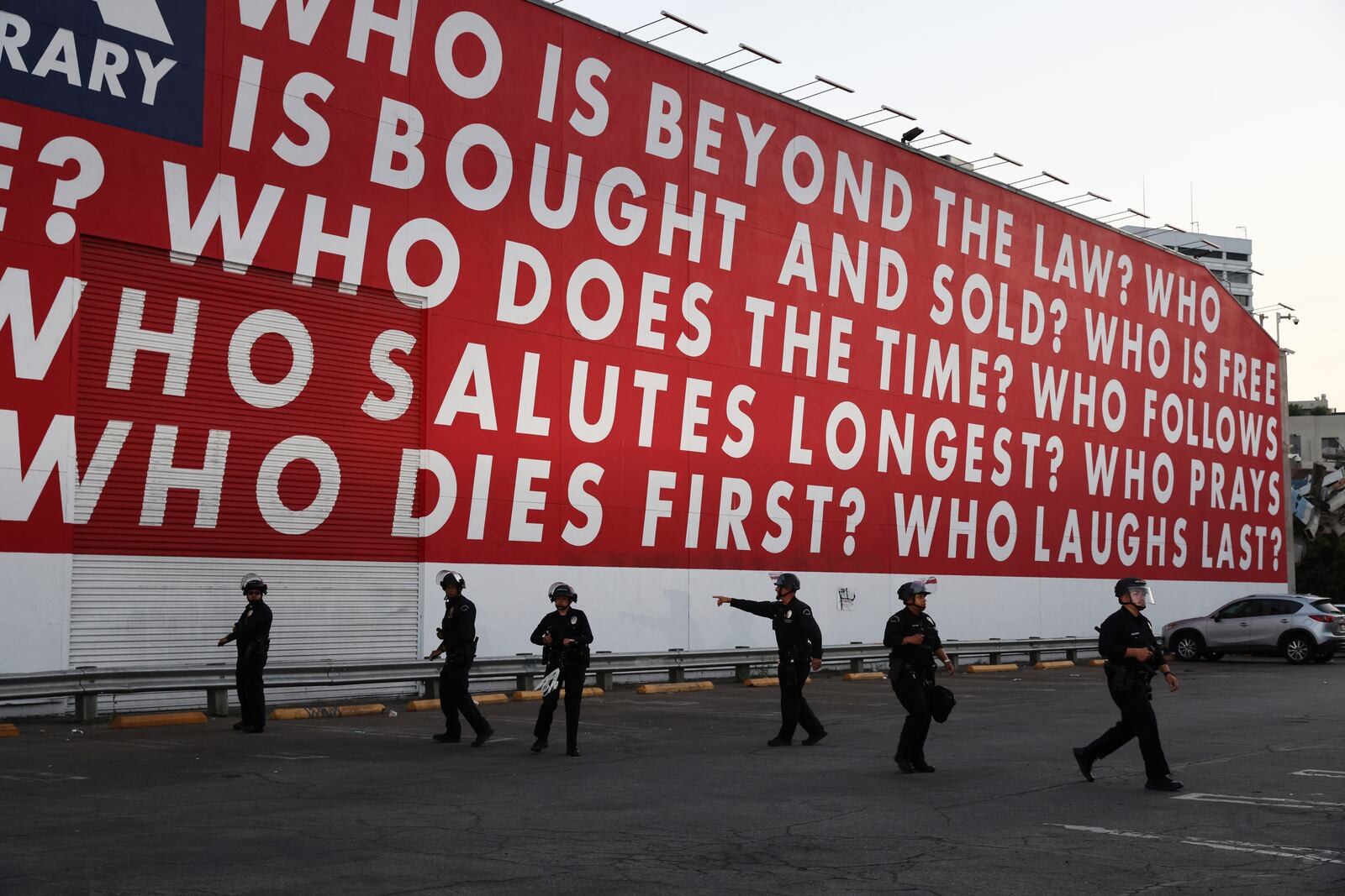 Los Angeles police officers form up beneath a mural by artist Barbara Kruger while protesters rally during a demonstration in response to a series of United States Immigration and Customs Enforcement (ICE) raids throughout the country, in Los Angeles, Calif., Thursday, June 12, 2025. (Gabrielle Lurie/San Francisco Chronicle via AP)
