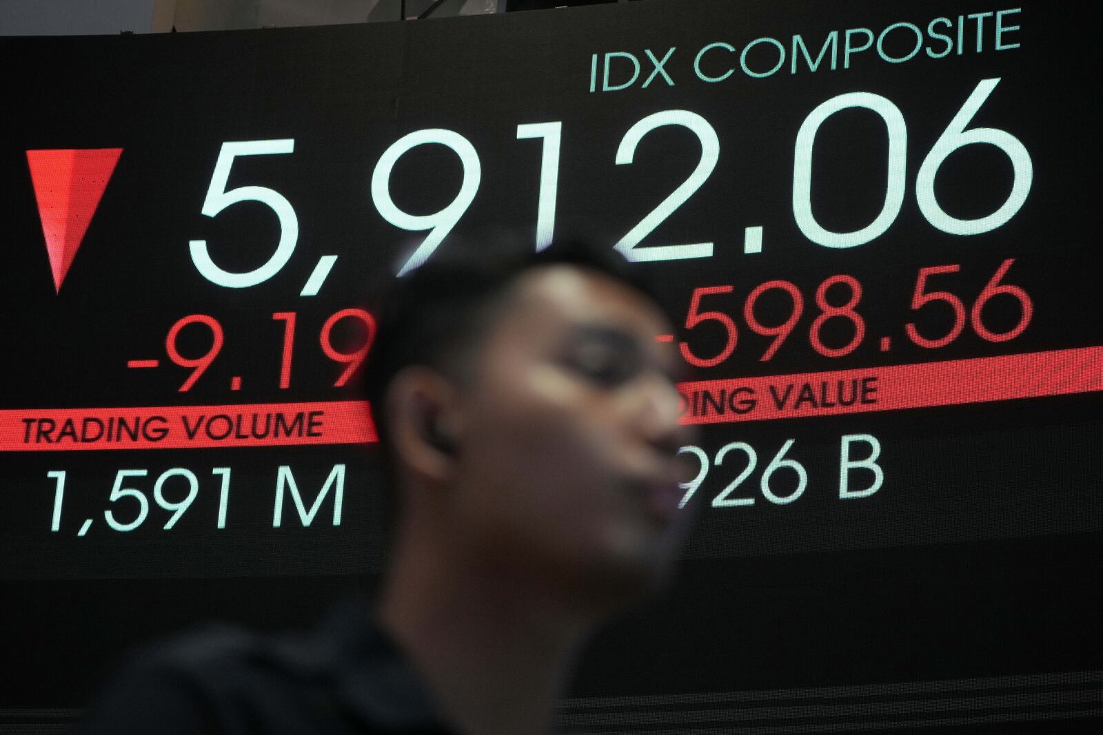 A man stands near an electronic board displaying stock prices at the Indonesia Stock Exchange, in Jakarta, Indonesia, Tuesday, April 8, 2025. (AP Photo/Achmad Ibrahim)