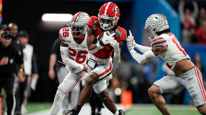 FILE - Georgia wide receiver Adonai Mitchell, center, makes a catch against Ohio State cornerback Cameron Brown (26) during the first half of the Peach Bowl NCAA college football semifinal playoff game Dec. 31, 2022, in Atlanta. Texas receiver Adonai Mitchell could have stayed at Georgia where he was already a hero. He had two of the biggest catches in program history in help the Bulldogs to the last two national championships. But the coos and cuddles of a toddler daughter drew him home to Texas. (AP Photo/John Bazemore, File)