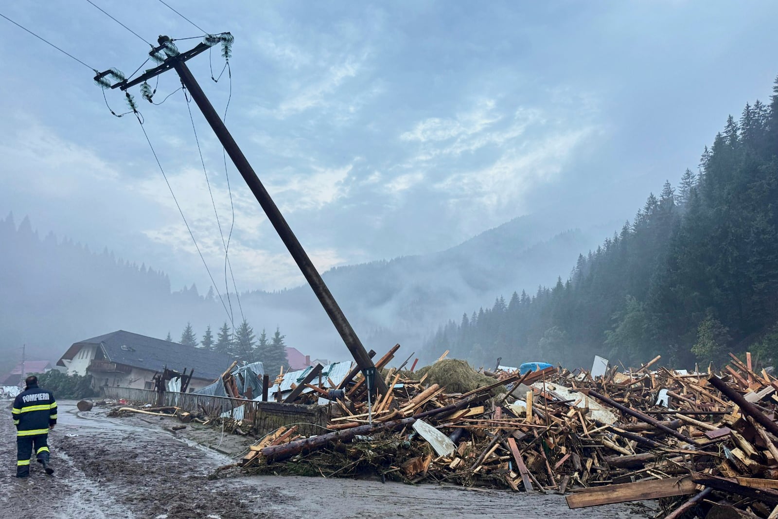 In this image released by the Romanian Emergency Services Suceava (ISU Suceava) first responders walk by damaged vehicles after a flash flood in the village of Brosteni, northern Romania, Monday, July 28, 2025. (Romanian Emergency Services - ISU Suceava via AP)
