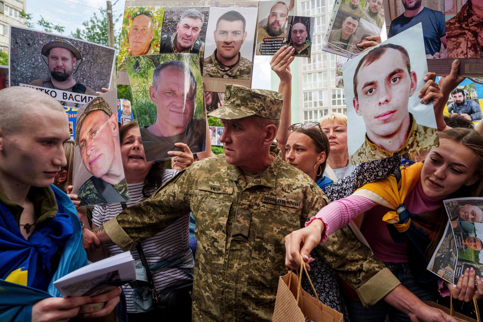 An Ukrainian soldier, left, walks though human corridor with people holding photos of their missed relatives after returning from captivity after a POWs exchange between Russia and Ukraine, in Chernyhiv region, Ukraine, Monday, June 9, 2025. (AP Photo/Evgeniy Maloletka)