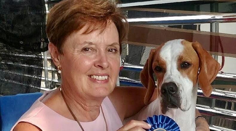 Dr. Patricia Haines smiles posing with a blue ribbon and a brown and white Pointer dog.