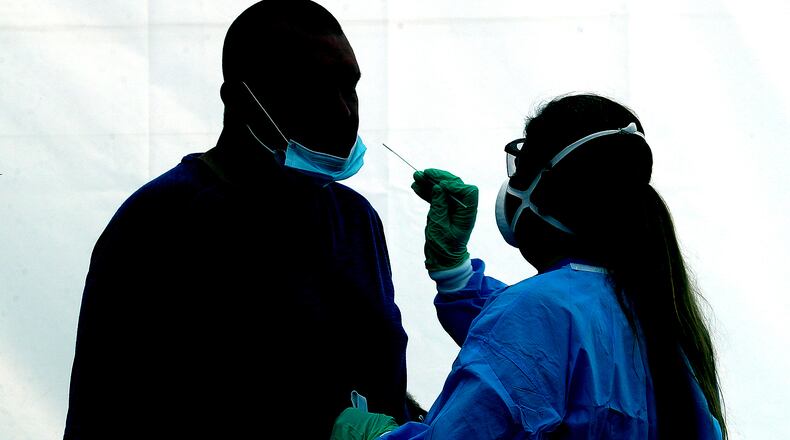A man is silhoutted against the wall of a white tent, illuminated by the sun, as he gets a COVID-19 test Wednesday at the Clark County Combined Health District's free COVID testing clinic at Hayward Middle School.