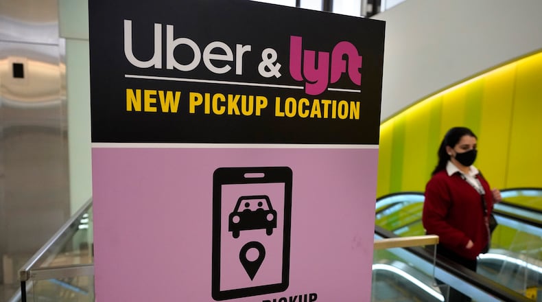FILE - In this Feb. 9, 2021 file photo, a passer-by walks past a sign offering directions to an Uber and Lyft ride pickup location at Logan International Airport, in Boston.