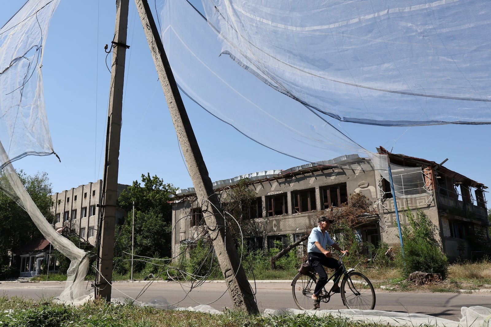 FILE - In this photo provided by Ukraine's 65th Mechanized Brigade press service, a resident rides a bike along the street under an anti-drone net in Orikhiv in Ukraine’s Zaporizhzhia region, July 15, 2025. (Andriy Andriyenko/Ukraine's 65th Mechanized Brigade via AP, File)