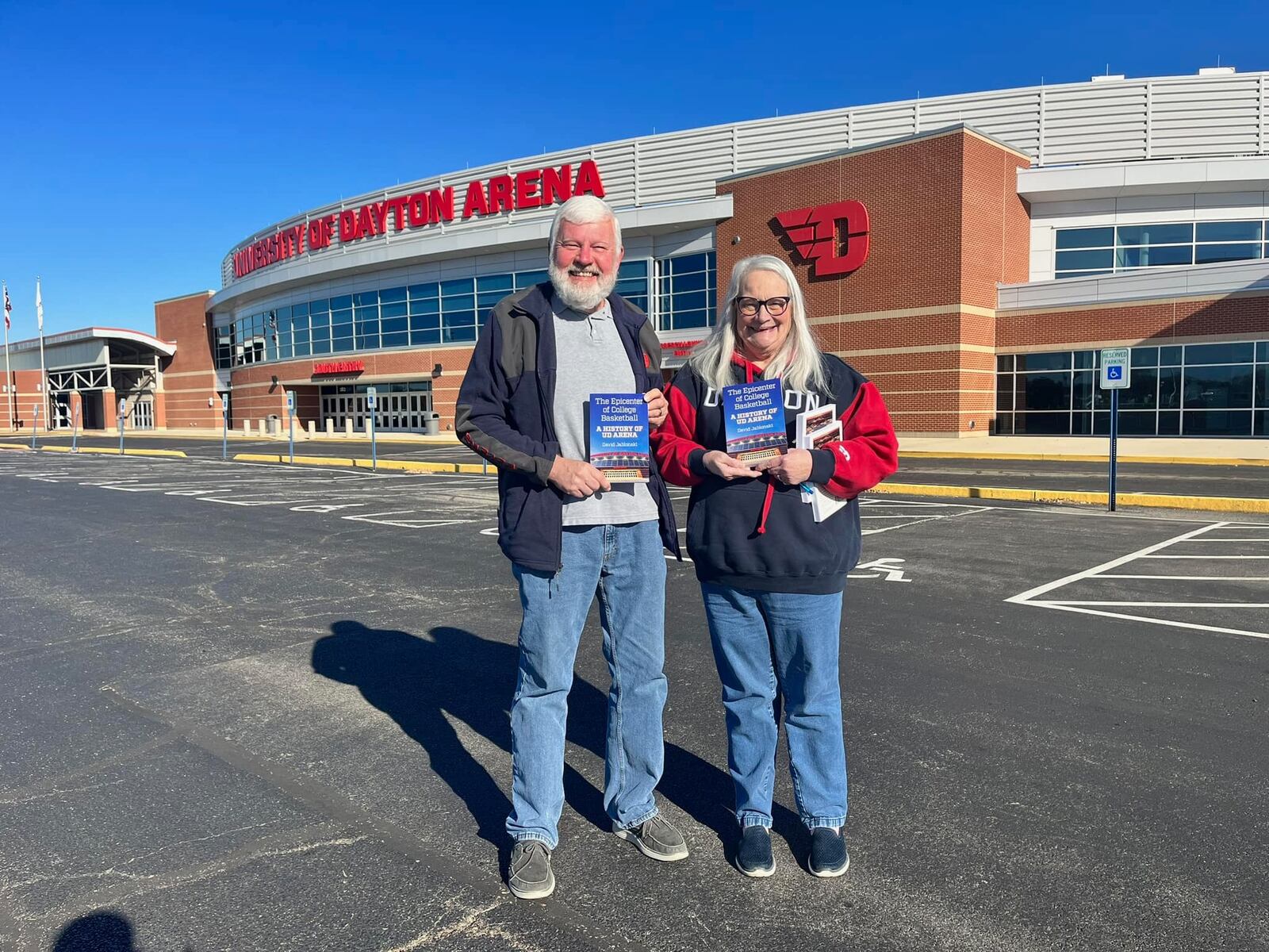 Kurt and Rita Rinehart show off copies of "The Epicenter of College Basketball: A History of UD Arena" in front of the arena on Tuesday, Nov. 14, 2023, in Dayton. David Jablonski/Staff