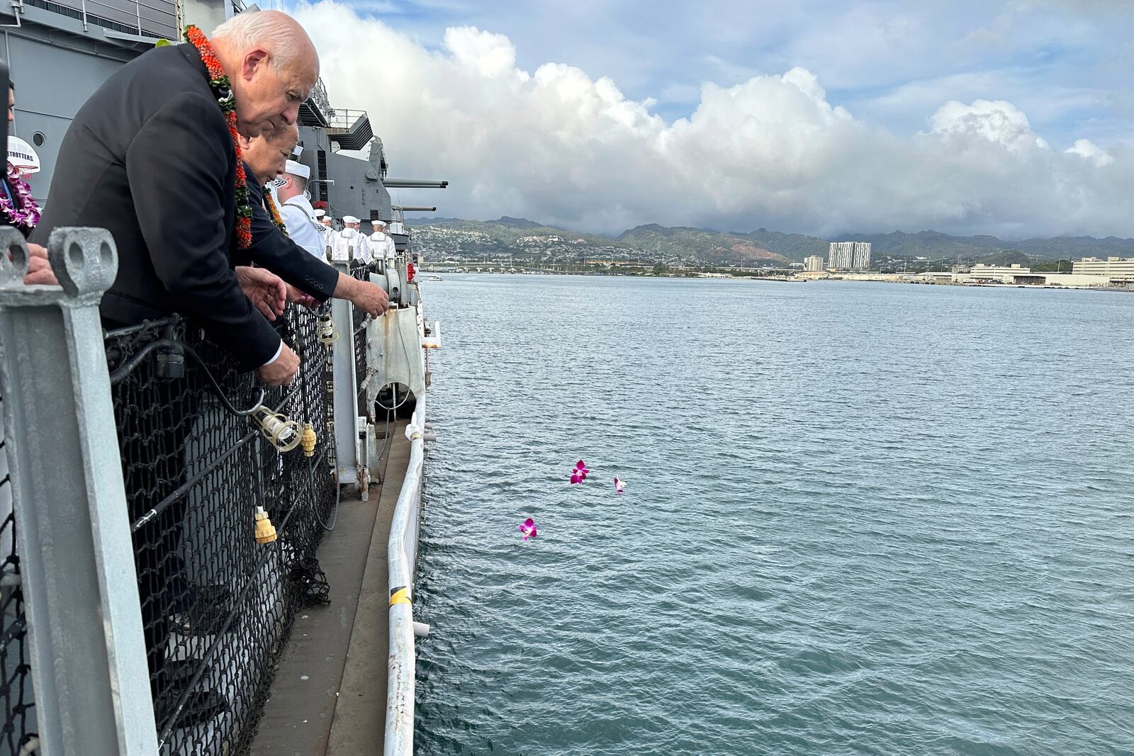 Honolulu Mayor Rick Blangiardi, front left, and Minamikyushu Mayor Hiroyuki Nuruki, behind, toss flower petals into the ocean from the Battleship Missouri Memorial during a ceremony marking the 80th anniversary of the 1945 kamikaze attack on the USS Missouri and subsequent burial at sea of the Japanese pilot, Friday, April 11, 2025, in Pearl Harbor, Hawaii. (AP Photo/Audrey McAvoy)