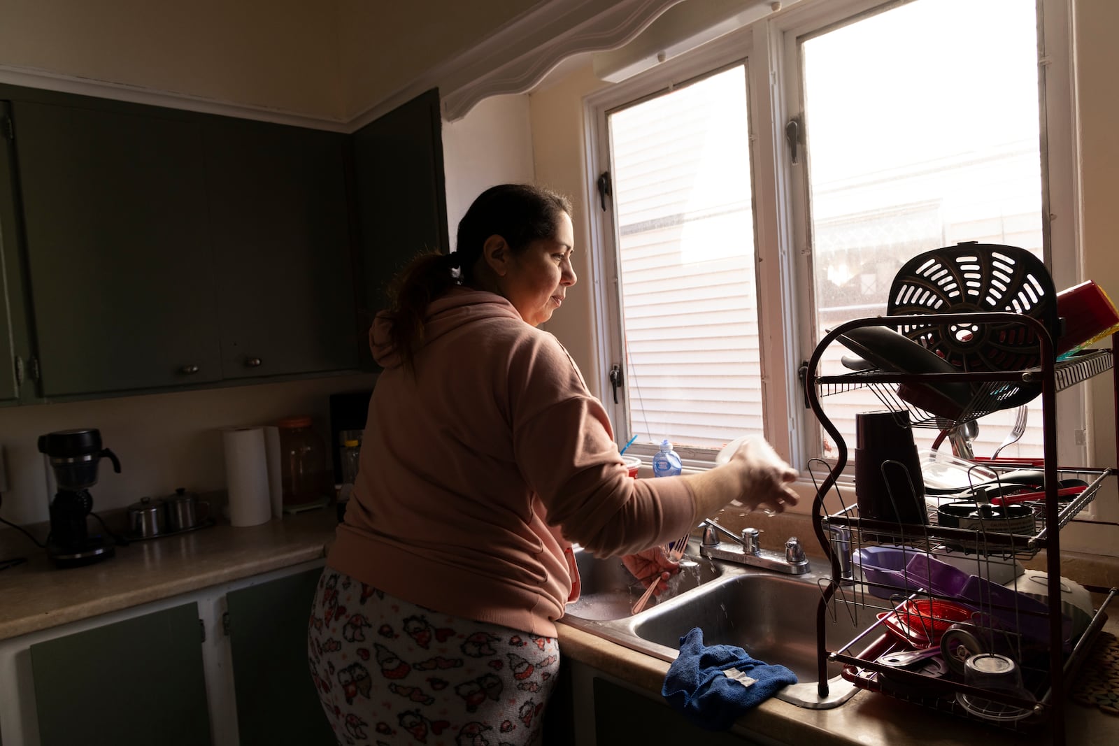 Arelis Ayala washes dishes while making breakfast for her family on Sunday, March 23, 2025, in Rochester, N.Y. (Toni Duncan via AP)
