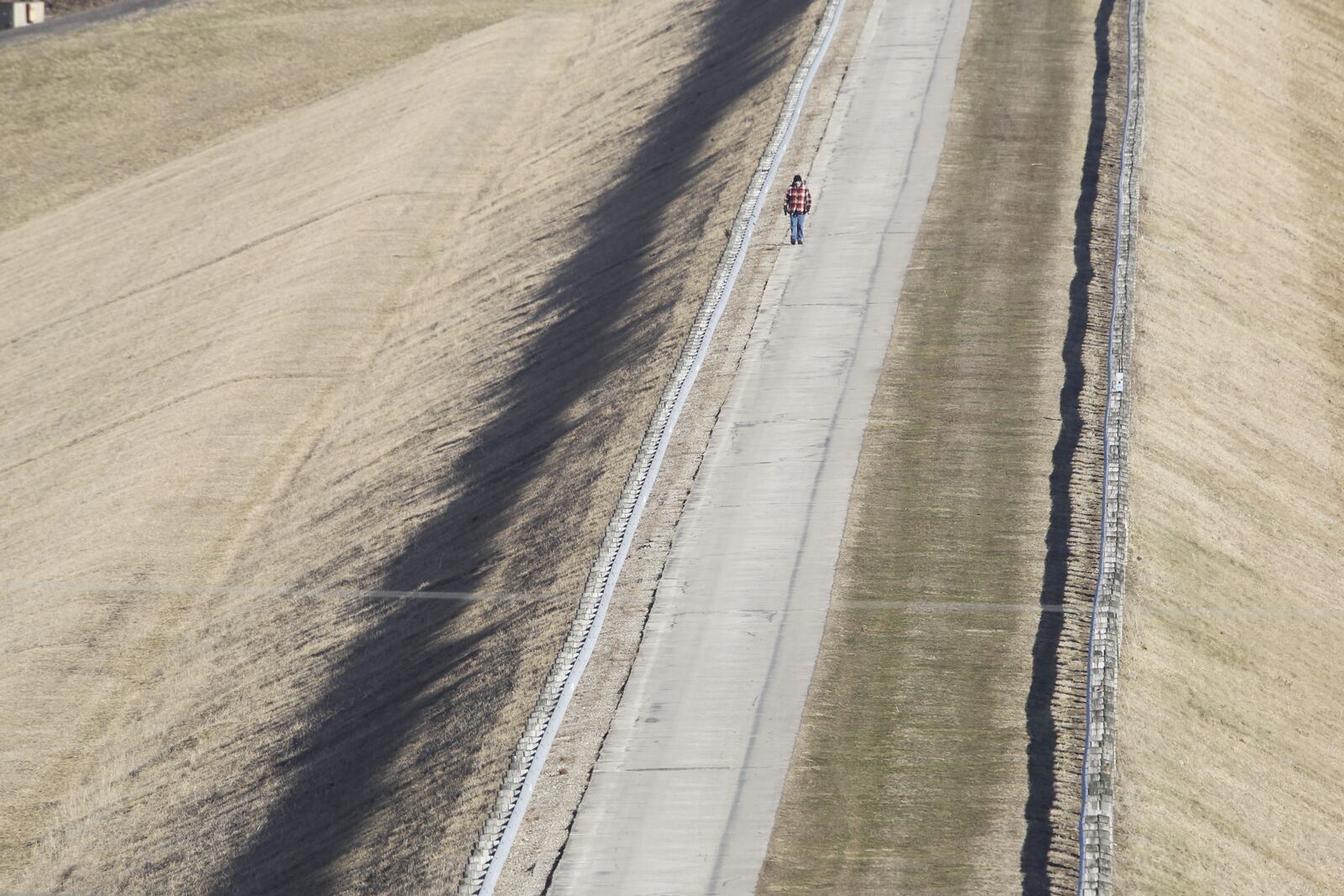 A walker crosses Huffman Dam on a sunny winter morning.  The dam on the Mad River was completed in 1921 as part of a flood control project to prevent another flood like Dayton experienced in 1913.  The dam is part of Huffman Reserve which was opened to the public on April 1, 1967 and is part of Five Rivers MetroParks. TY GREENLEES / STAFF