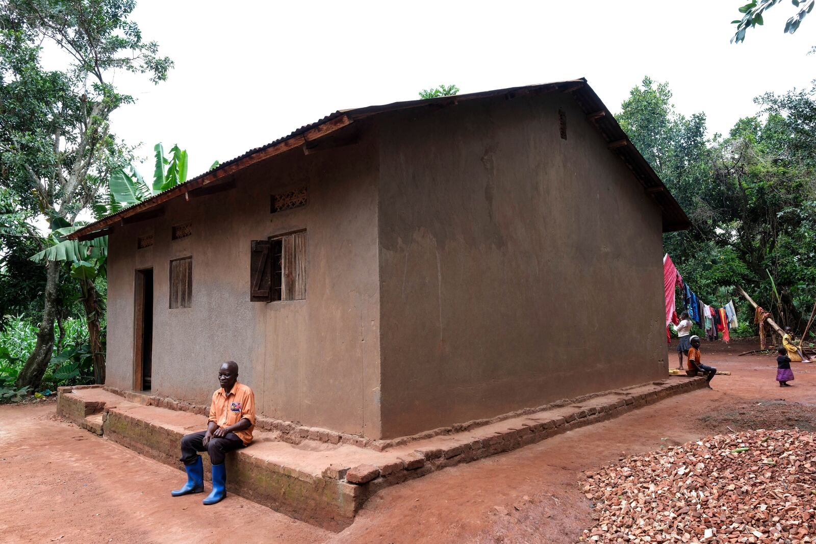 Simon Tigawalana rests in front of his house with clay-based earthen floors by EarthEnable on May 16, 2025, in Jinja, Uganda. (AP Photo/Hajarah Nalwadda)