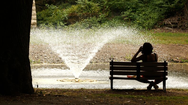 A woman finds relief from the heat on a park bench in the shade while she watches the fountain in the middle of the Snyder Park Lagoon. BILL LACKEY/STAFF