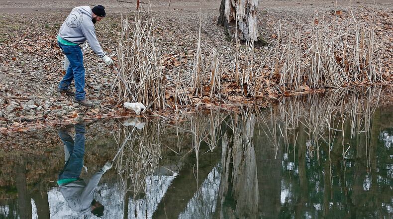 Ethan Ford, an employee of National Trail Parks and Recreation, is reflected in one of the ponds in Snyder Park as he picks up litter along the shoreline Friday, Feb. 10, 2023. BILL LACKEY/STAFF