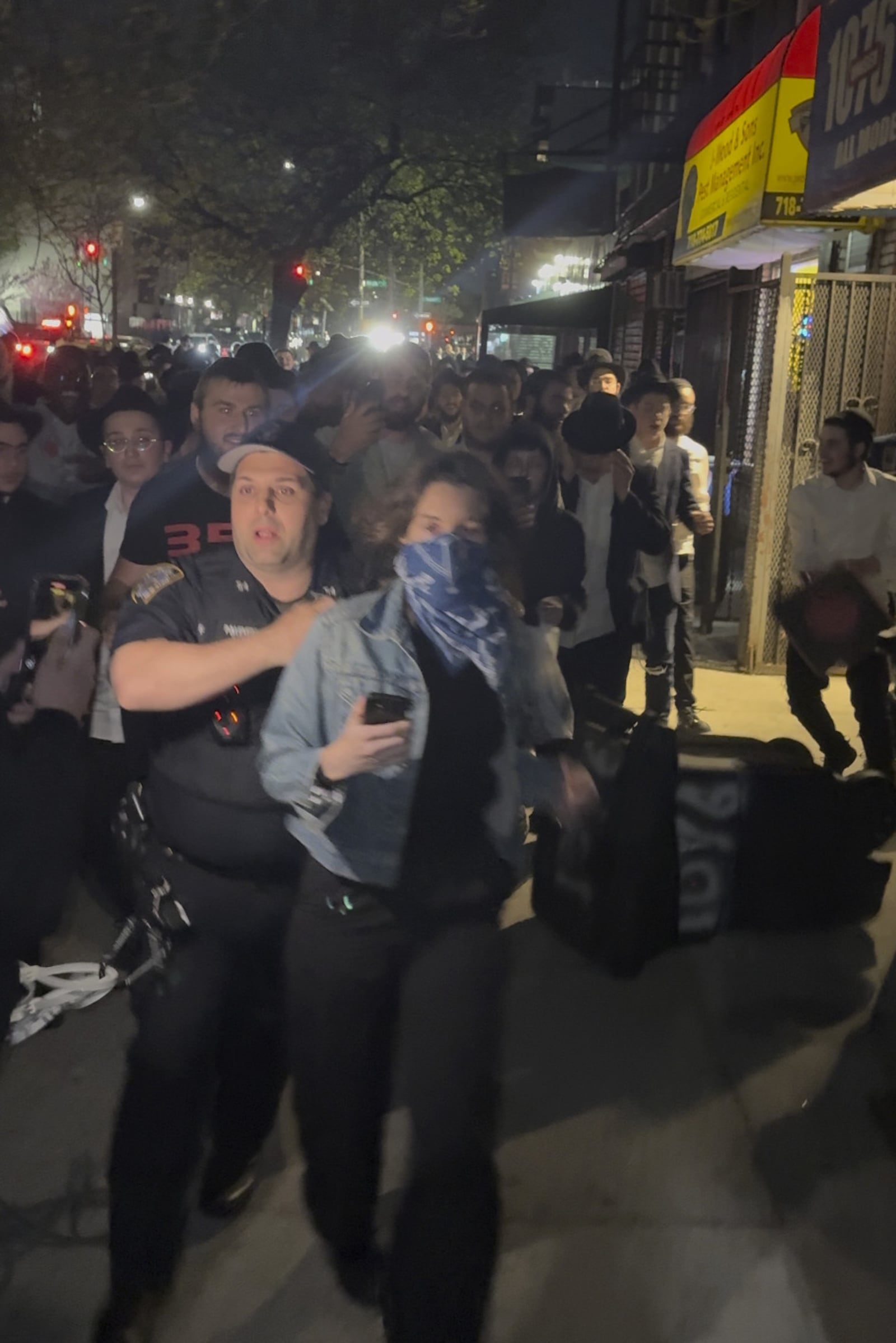 This image taken from video shows a woman and a police officer as they are pursued by a crowd of men in the Crown Heights section of Brooklyn, N.Y., on Thursday, April 24, 2025. (AP Photo)