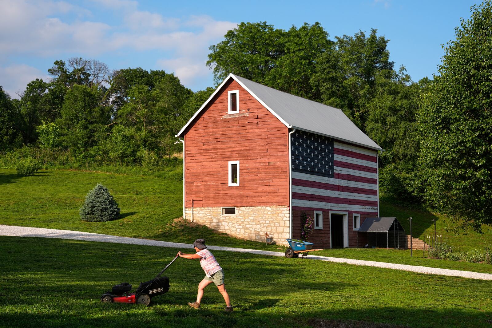 Stacey Schmitt mows in front of a flag-painted barn Saturday, June 7, 2025, on her family farm near Linwood, Kan. (AP Photo/Charlie Riedel)