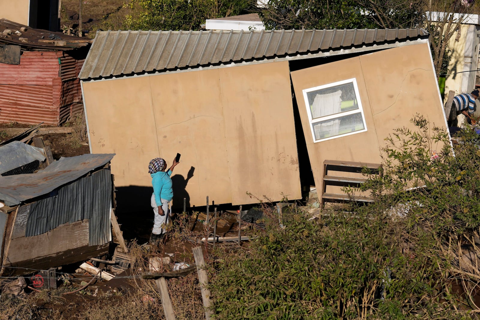 A woman takes a photograph of her damaged house, after floods swept through the area in Mthatha, South Africa, Thursday, June 12, 2025. (AP Photo/Themba Hadebe)