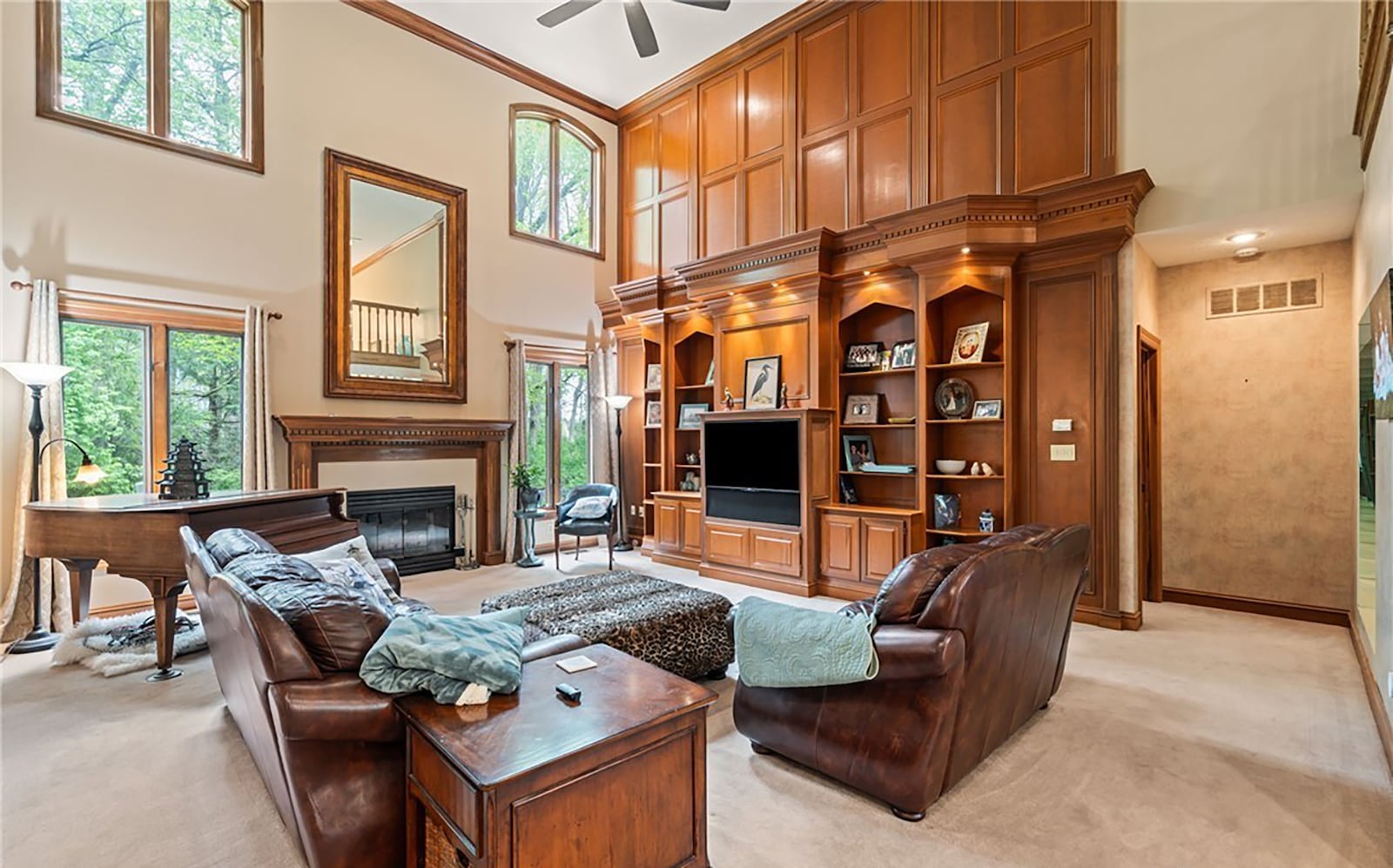 The two story great room has a ceiling fan, neutral carpet, crown molding and a built in floor to ceiling wood entertainment unit with bookcases and lighting. There is also a woodburning fireplace.