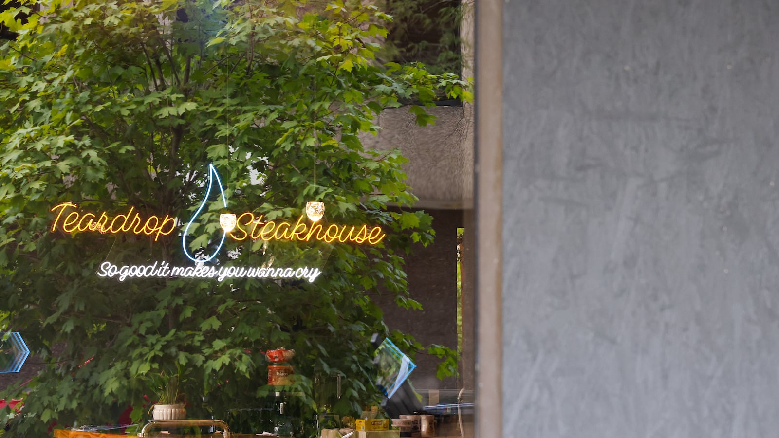 An electric sign inside Teardrops Steakhouse is visible through a window with trees reflecting on Tuesday, Aug. 12. The window beside it replaced with a wooden board painted black. The glass window was damaged due to vandalism. BRYANT BILLING / STAFF