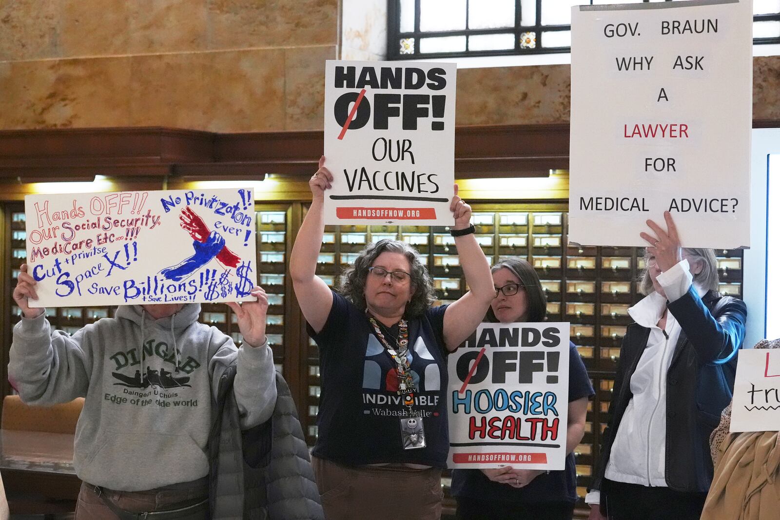 Protesters hold up signs outside of the Make Indiana Healthy Again initiative event in Indianapolis, Tuesday, April 15, 2025. (AP Photo/Michael Conroy)