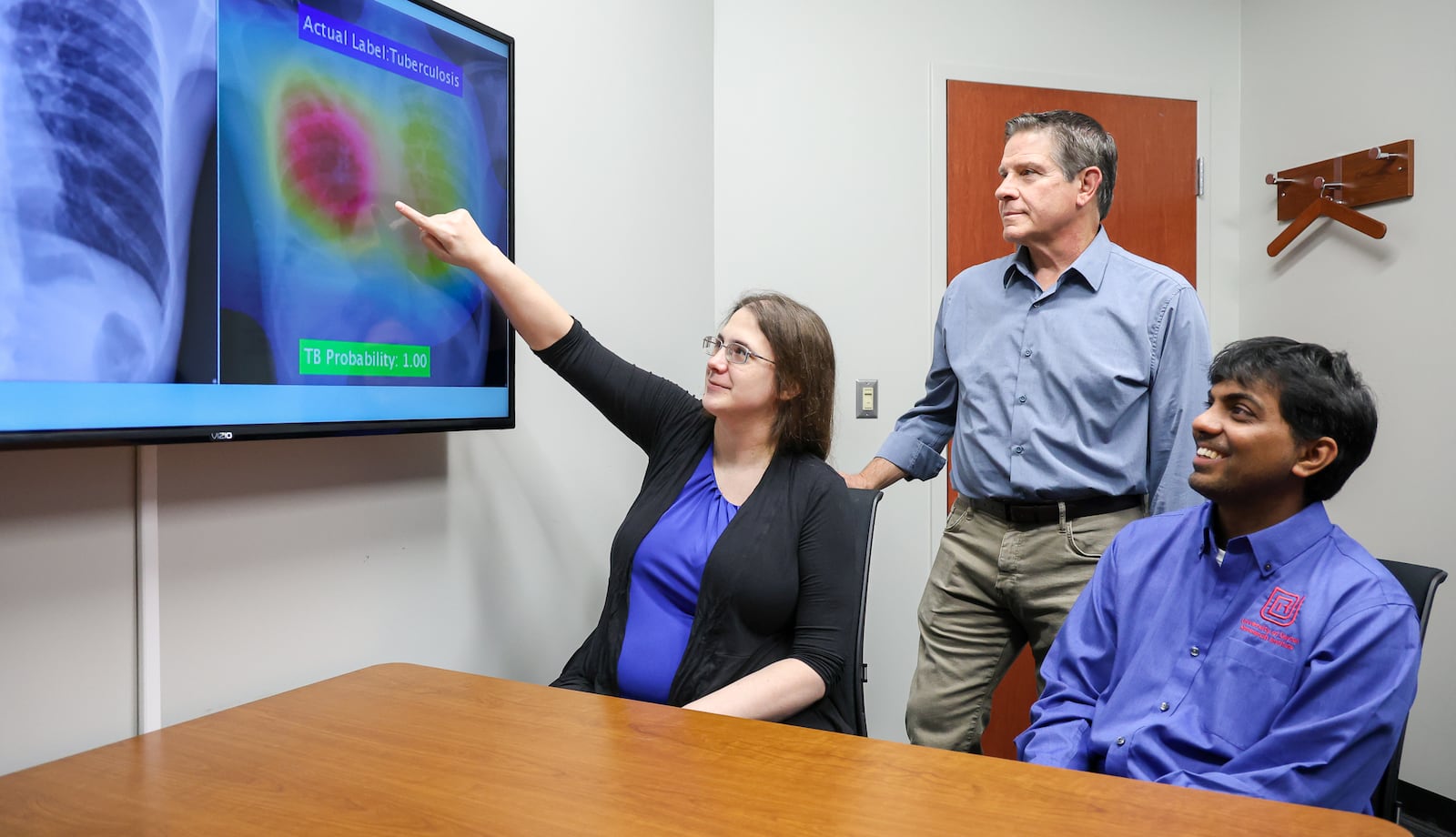 From left to right, Kelly Beigh, Christopher Ristich and Barath Narayanan pose at University of Dayton Research Institute in front of a television showing one X-rays of a patient with tuberculosis used for artificial intelligence software that Narayan developed to help health care professionals diagnosis the illness. Narayanan is a senior software scientist, Beigh is a team lead senior software engineer and Ristich is executive director of digital and systems engineering. BRYANT BILLING / STAFF