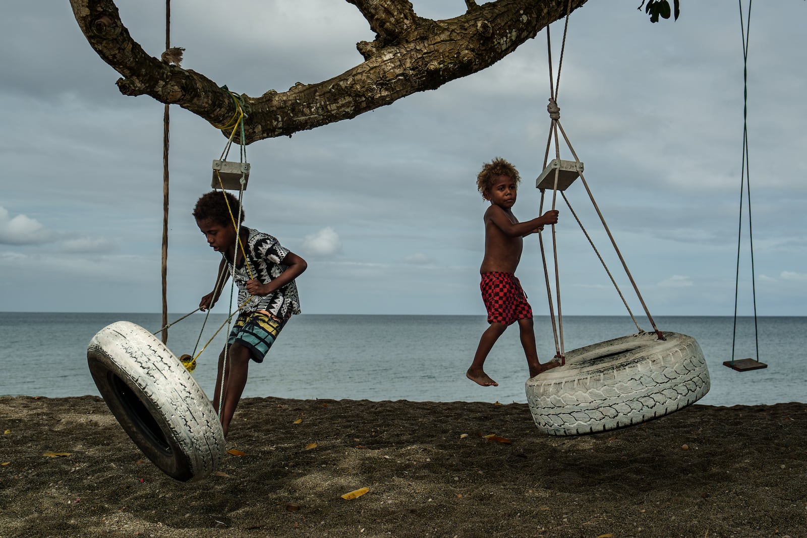 Children play on an uprooted tree along a beach in Mele, Vanuatu that was once lined with vegetation, now largely lost to storms, erosion and other environmental pressures on Saturday, July 19, 2025. (AP Photo/Annika Hammerschlag)