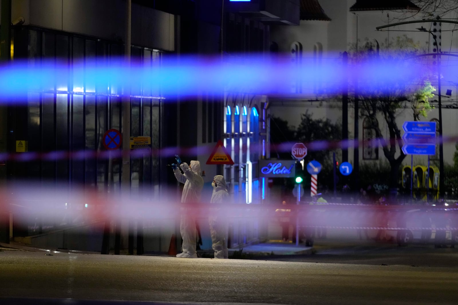 Police investigators wearing coveralls inspect the site after a bomb explosion outside of the Hellenic Train offices the company that runs Greece's railway, the first building on the left, in Athens, Greece, Friday, April 11, 2025. (AP Photo/Petros Giannakouris)