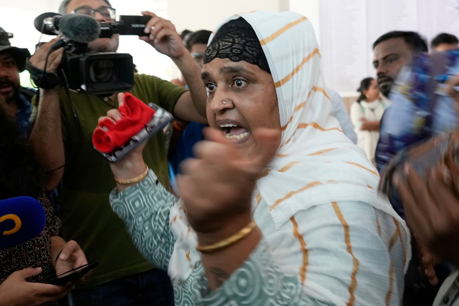 Salma Rafiq Memon, in white scarf, gestures angrily as she speaks to media personnel while waiting for the bodies of four relatives who died in the Air India plane crash, at a hospital in Ahmedabad, India, Saturday, June 14, 2025. (AP Photo/Rafiq Maqbool)