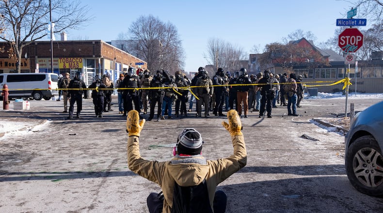 A protester sits on the street with his arms up in front of federal agents in Minneapolis, on Saturday, Jan. 24, 2026. (Alex Kormann/Star Tribune via AP)