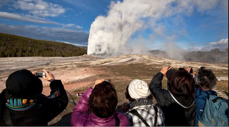 In this May 2011 file photo, tourists photograph Old Faithful erupting on schedule in Yellowstone National Park, Wyo. On Tuesday, March 24, 2020, the National Park Service announced that Yellowstone and Grand Teton National Parks would be closed until further notice, and no visitor access will be permitted to either park. (AP Photo/Julie Jacobson, File)
