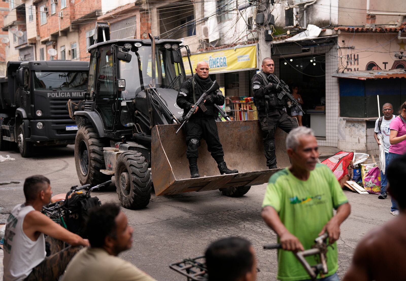 FILE - Police ride past residents in a bulldozer they use to clear street barricades during a security operation against organized crime in the Mare Complex favela of Rio de Janeiro, Brazil, Oct. 9, 2023. (AP Photo/Silvia Izquierdo, File)