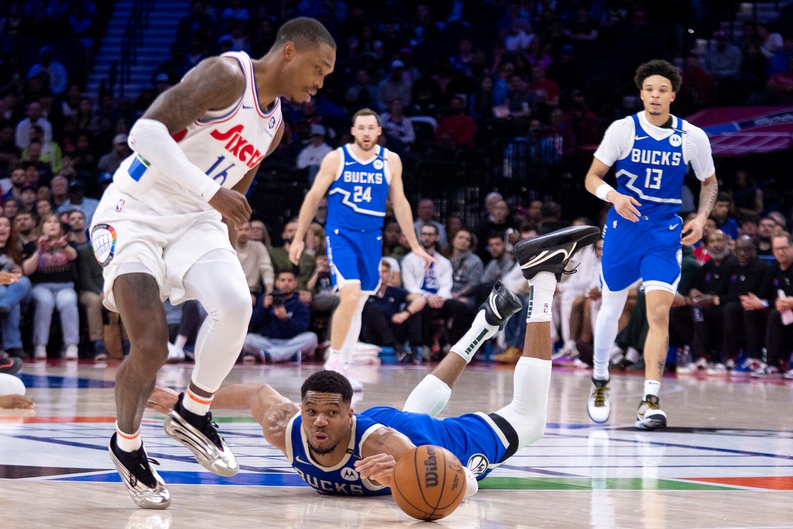 Milwaukee Bucks' Giannis Antetokounmpo, center, dives for the loose ball with Philadelphia 76ers' Lonnie Walker IV, left, looking on during the first half of an NBA basketball game, Thursday, April 3, 2025, in Philadelphia. (AP Photo/Chris Szagola)