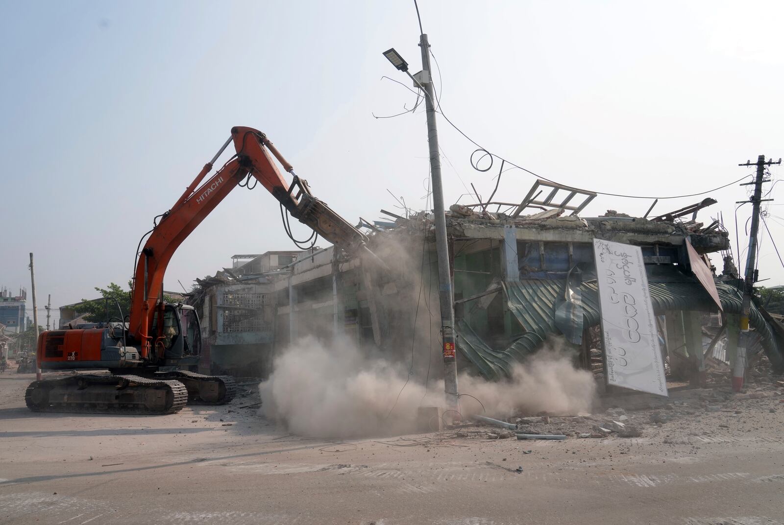 A volunteer drives a backhoe to clear debris of a building at a market, after one month of the strong earthquake in Naypyitaw, Myanmar, Monday, April 28, 2025. (AP Photo/Aung Shine Oo)