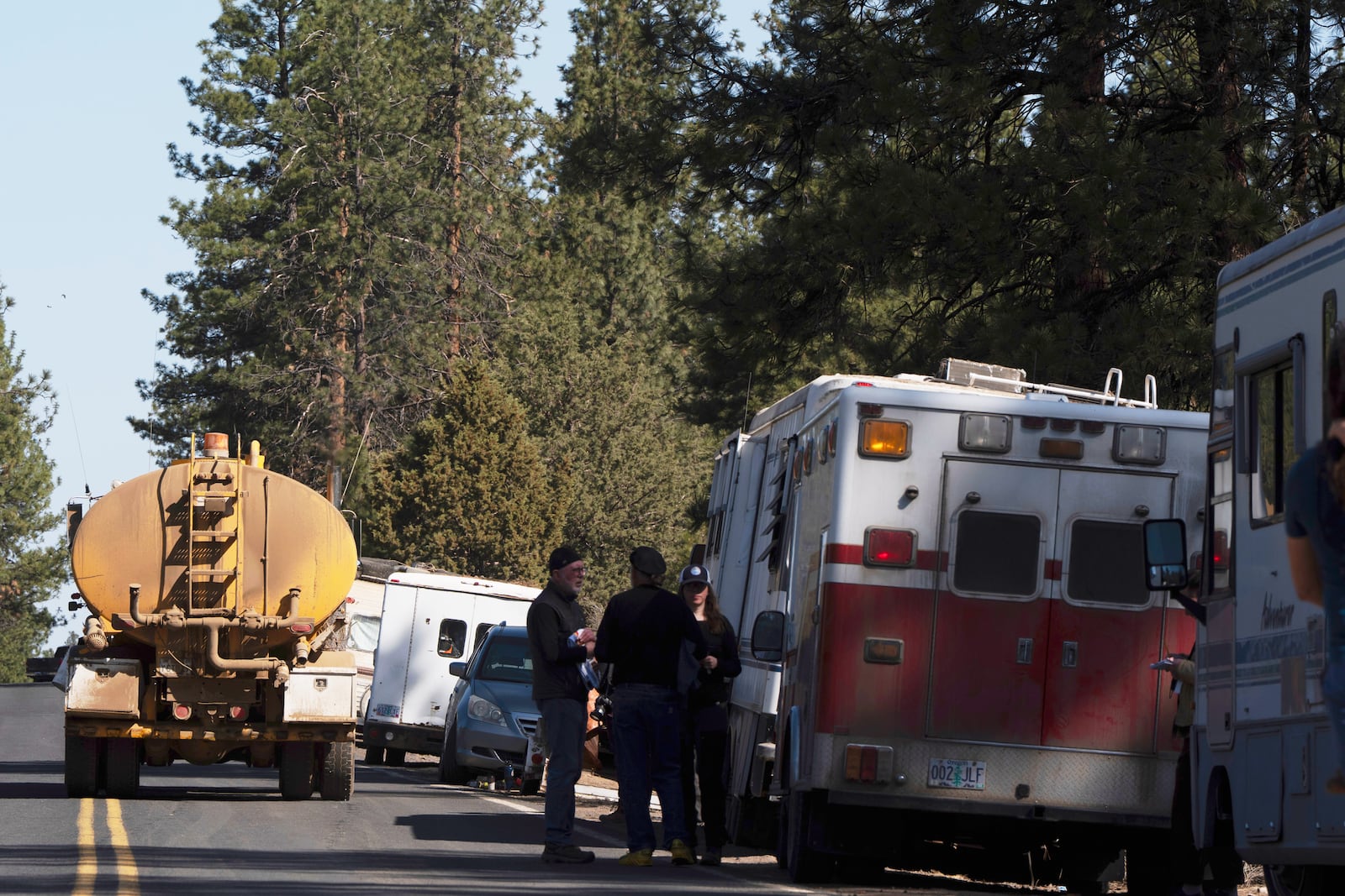 A trucking and logging vehicle, at left, drives past trailers lining China Hat Road as leaves an area that was closed off in Deschutes National Forest, Thursday, May 1, 2025 near Bend, Ore. (AP Photo/Jenny Kane)