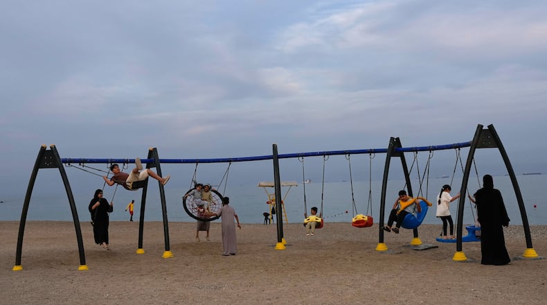 Children and adults play on swings on the beach as oil tankers and cargo ships line up in the Strait of Hormuz near Khor Fakkan, United Arab Emirates, Wednesday, March 11, 2026. (AP Photo/Altaf Qadri)
