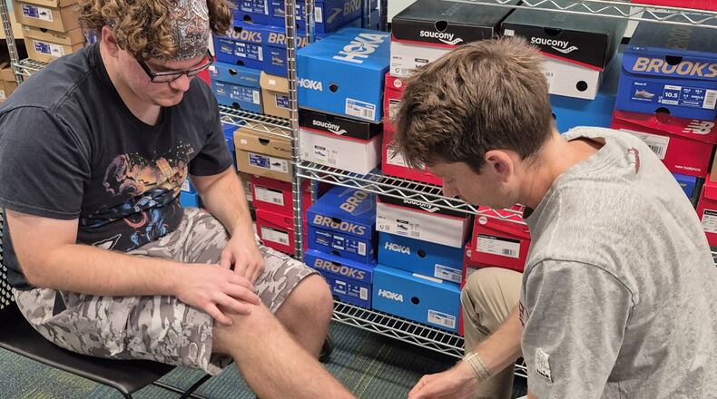 Marshall Stearns (left) is fitted with a new pair of tennis shoes by Max Hoffman, a Diadora sales representative with Up and Running Dayton, during a shoe giveaway at Daybreak on Monday. MICHAEL KURTZ / STAFF