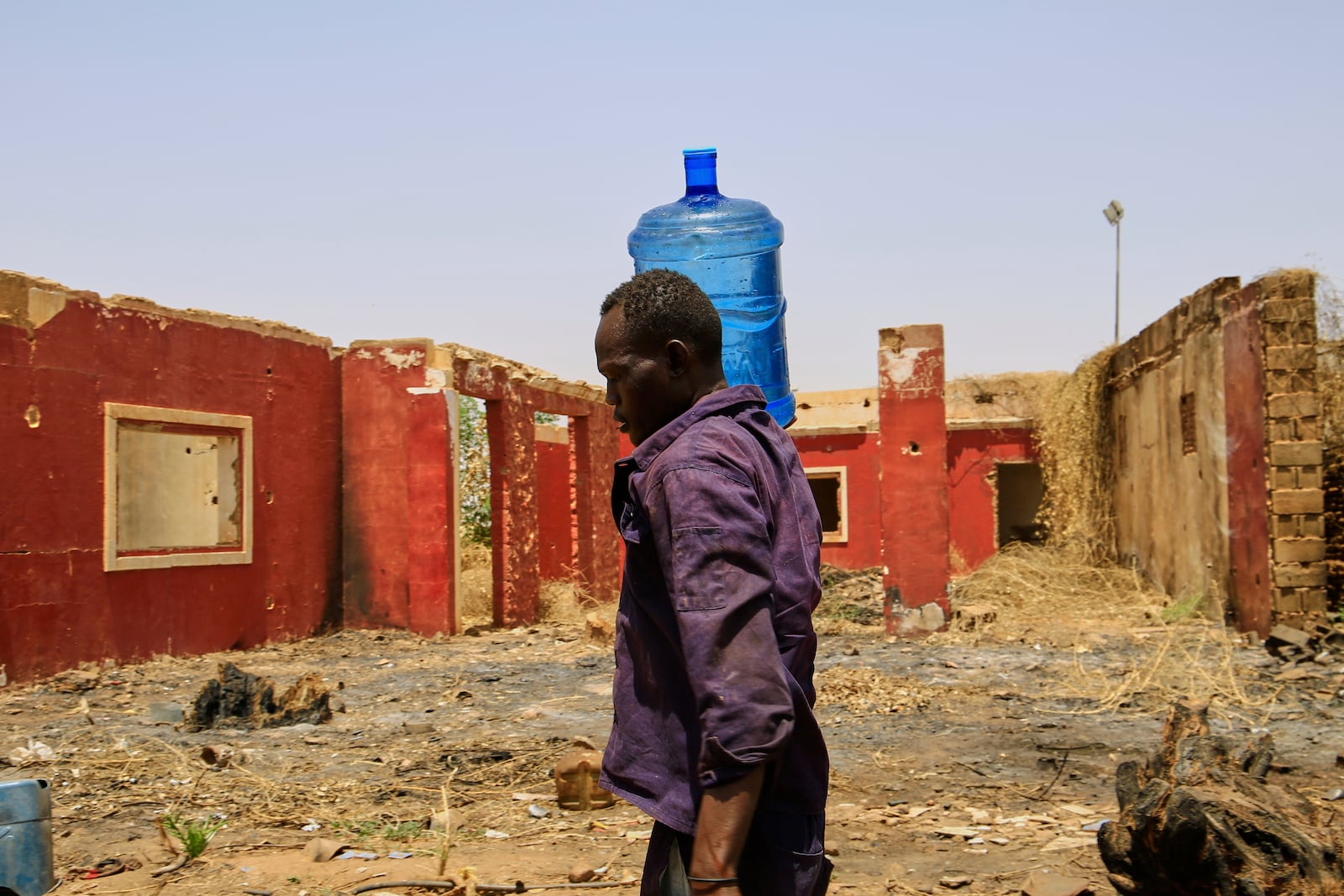 A man carries a water container past a building damaged during the civil war at a distribution point due to water outages in Khartoum, Sudan, Sunday, May 25, 2025. (AP Photo)