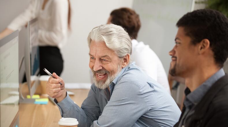 Smiling senior employee discussing email with colleague at workplace. Source: Shutterstock.