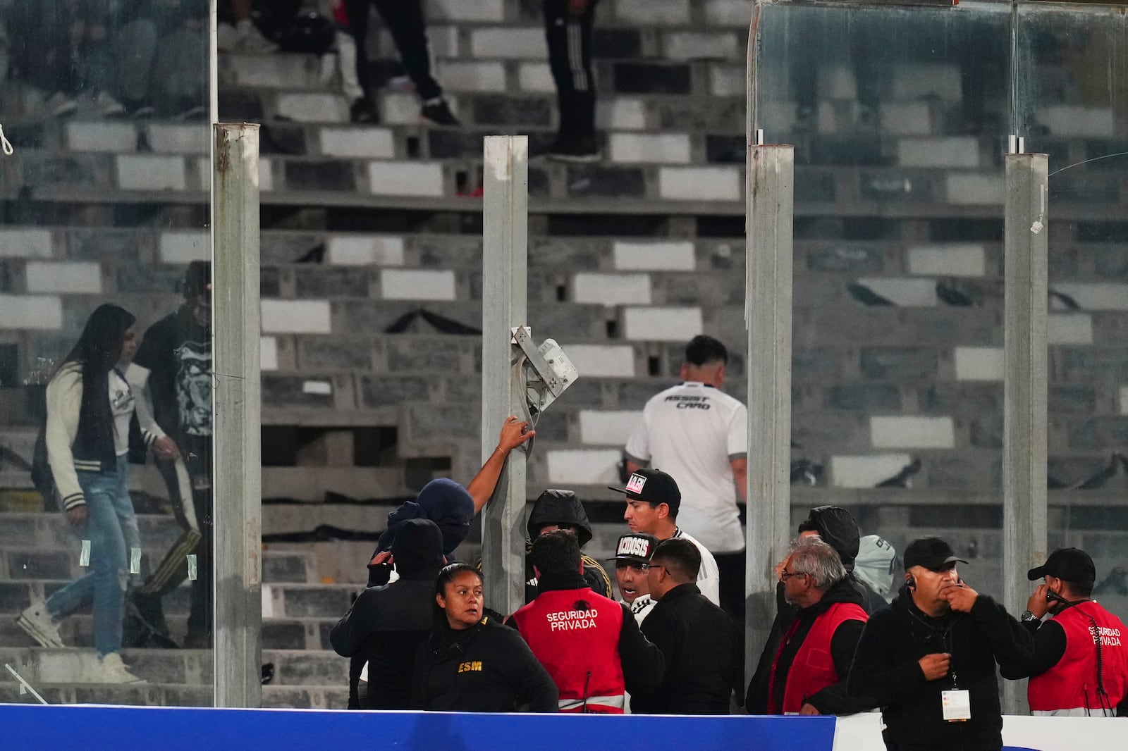 Security stewards confront fans after glass panels were broken and people invaded the field during a Copa Libertadores Group E soccer match against Brazil's Fortaleza at Monumental Stadium in Santiago, Chile, Thursday, April 10, 2025. (AP Photo/Esteban Felix)